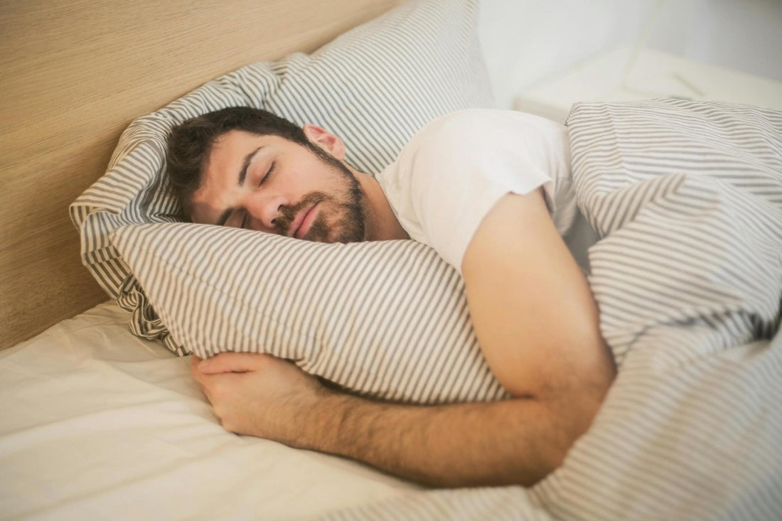 A man sleeps comfortably on his side, resting his head on a soft stripy gray pillow